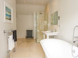 A bathroom with a bathtub, double sinks, a glass shower enclosure, a radiator with a towel, and a framed picture on the wall at Tan Llan in Llanelltyd near Dolgellau