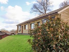 A log cabin with windows and a door on a grassy hill with shrubs in the foreground