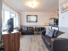 A living room with two sofas a dining table with chairs a television on a wooden stand and a kitchen area at Cove View in Ilfracombe