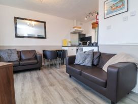 A living room with two brown leather sofas a dining table with four black chairs and a kitchenette at Cove View in Ilfracombe