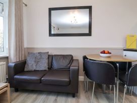 A living area with a brown leather sofa and a round dining table with black chairs at Cove View in Ilfracombe