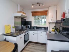 A kitchen with white cabinets black countertops a gas stove microwave sink and a wooden table at Cove View in Ilfracombe