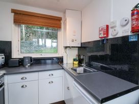A kitchen with white cabinets a sink a kettle toaster microwave and a window showing greenery at Cove View in Ilfracombe