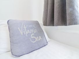 A pillow with the text in need of vitamin sea on a bed next to a grey curtain at Cove View in Ilfracombe