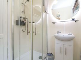 A bathroom with a glass shower enclosure and a white sink cabinet with a round mirror above at Cove View in Ilfracombe