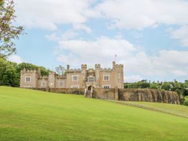 A large stone castle with battlements and towers on a grassy hill with trees in the background