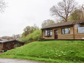 A wooden cabin with a bench on a grassy hill surrounded by trees at Cove View in Ilfracombe