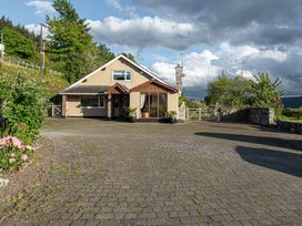 A driveway with cobblestone paving leading to a house with large windows and a wooden porch at Cilfan in Llanrwst