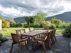 An outdoor patio with a wooden table and eight wooden chairs with garden and hills in the background at Cilfan in Llanrwst