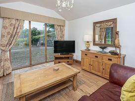 A living room with wooden furniture a television and a large window with floral curtains at Cilfan in Llanrwst