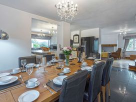 A dining room with a wooden table set with plates glasses and cutlery next to a kitchen and living area at Cilfan in Llanrwst