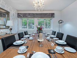 A dining room with a wooden table set with white dishes black chairs and a chandelier at Cilfan in Llanrwst