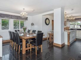 A dining area with a wooden table set with plates and glasses and black chairs next to a kitchen with an island and bar stools at Cilfan in Llanrwst