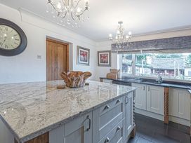 A kitchen with a large marble island, chandeliers, wooden door, wall clock, framed art, and window over the sink at Cilfan Llanrwst
