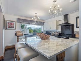 A kitchen with marble island counter stools chandeliers and a window showing trees and hills at Cilfan in Llanrwst