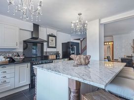 A kitchen with a marble island countertop black appliances chandeliers and wooden stools at Cilfan in Llanrwst