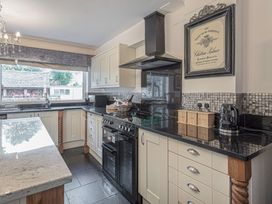 A kitchen with black countertops white cabinets a black stove and oven a kettle and a framed wine poster on the wall at Cilfan in Llanrwst
