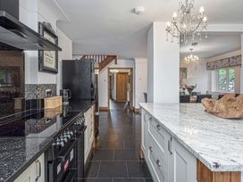 A kitchen with a black stove and refrigerator a white island with a granite countertop and a wooden decorative piece a dining area with a chandelier and flowers on the table at Cilfan in Llanrwst