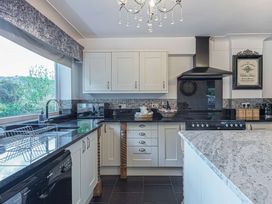 A kitchen with white cabinets black countertops a stove with a hood and a large window at Cilfan in Llanrwst