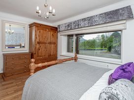 A bedroom with a wooden bed and furniture and a window showing trees at Cilfan in Llanrwst