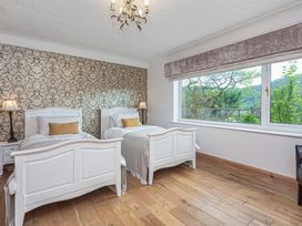 A bedroom with two white beds and bedside lamps by a window showing trees and hills at Cilfan in Llanrwst
