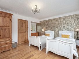 A bedroom with two white single beds wooden wardrobe and door with patterned wallpaper at Cilfan in Llanrwst