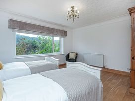 A bedroom with two single beds a window with a view of trees a chair and a wooden wardrobe at Cilfan in Llanrwst