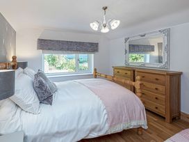 A bedroom with a wooden bed, dressers, a large mirror, and a window with a view at Cilfan in Llanrwst