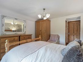 A bedroom with wooden furniture a bed a mirror a wardrobe an armchair and a wooden door at Cilfan in Llanrwst