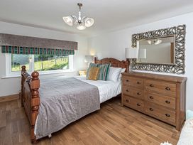 A bedroom with a wooden bed a wooden dresser a mirror and a window with striped blinds at Cilfan Llanrwst
