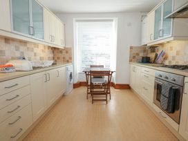 A kitchen with cabinets a washing machine a dining table with chairs and a stove at Captains Rest in Porthmadog