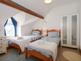 A bedroom with two single wooden beds a white wardrobe and a window with blue curtains at Captain's Rest in Porthmadog
