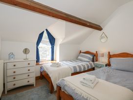 A bedroom with two single beds striped bedding a chest of drawers and a window with blue curtains at Captains Rest in Porthmadog