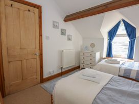 A bedroom with two single beds a door and a window with blue curtains at Captains Rest in Porthmadog
