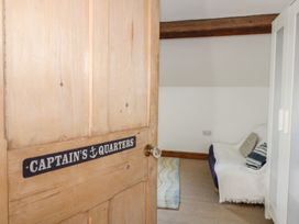 A partially open wooden door with a Captain's Quarters sign revealing a room with a sofa covered with a white throw and cushions beside a wardrobe at Captain's Rest in Porthmadog