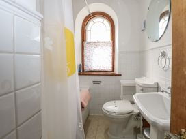 A bathroom with a toilet sink bathtub shower curtain and an arched window at Captains Rest in Porthmadog