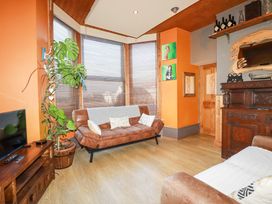 A living room with a brown leather sofa a wooden TV stand a large plant and orange walls at Mermaid's Rest in Newquay