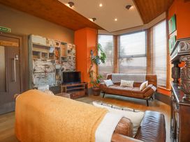 A living room with two brown sofas a wooden cabinet a television and large windows with blinds at Mermaid's Rest in Newquay