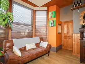 A sitting area with a brown leather couch and throw pillows next to windows with blinds at Mermaid's Rest in Newquay