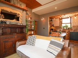A living room with a brown leather sofa and patterned cushions next to a wooden cabinet and a dining area with a wooden table and chairs at Mermaid's Rest in Newquay