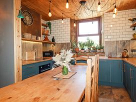 A kitchen with wooden table and chairs green cabinets plants on windowsill and hanging light bulbs at Mermaid's Rest in Newquay