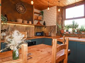 A kitchen with wooden cabinets a table chairs plants on the windowsill and a wall clock at Mermaids Rest in Newquay