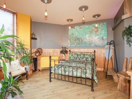 A bedroom with a metal bed frame with tropical bedding a beige chair plants wooden floor and an ironing board at Mermaids Rest in Newquay