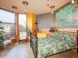 A bedroom with a metal bed with tropical print bedding plants near windows and wooden panel walls at Mermaids Rest in Newquay