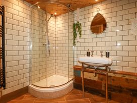 A bathroom with a corner shower enclosure a white sink a round mirror and hanging plants at Mermaid's Rest in Newquay