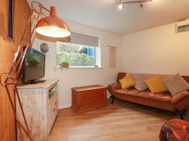A living room with a brown leather sofa yellow and beige cushions a wooden chest a white distressed cabinet with a television and a large copper lamp at The Aqua Shack in Newquay