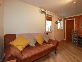 A brown couch with pillows next to a door and window in a room with wooden floor and dining table at The Aqua Shack in Newquay