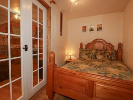A bedroom with a wooden bed and a nightstand lamp separated by glass doors from a kitchen area at The Aqua Shack in Newquay