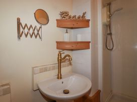 A bathroom with a white sink and brass faucet with wooden shelves and a shower at The Aqua Shack in Newquay