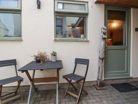 An outdoor seating area with a small table and two chairs next to a green door and windows at The Aqua Shack in Newquay